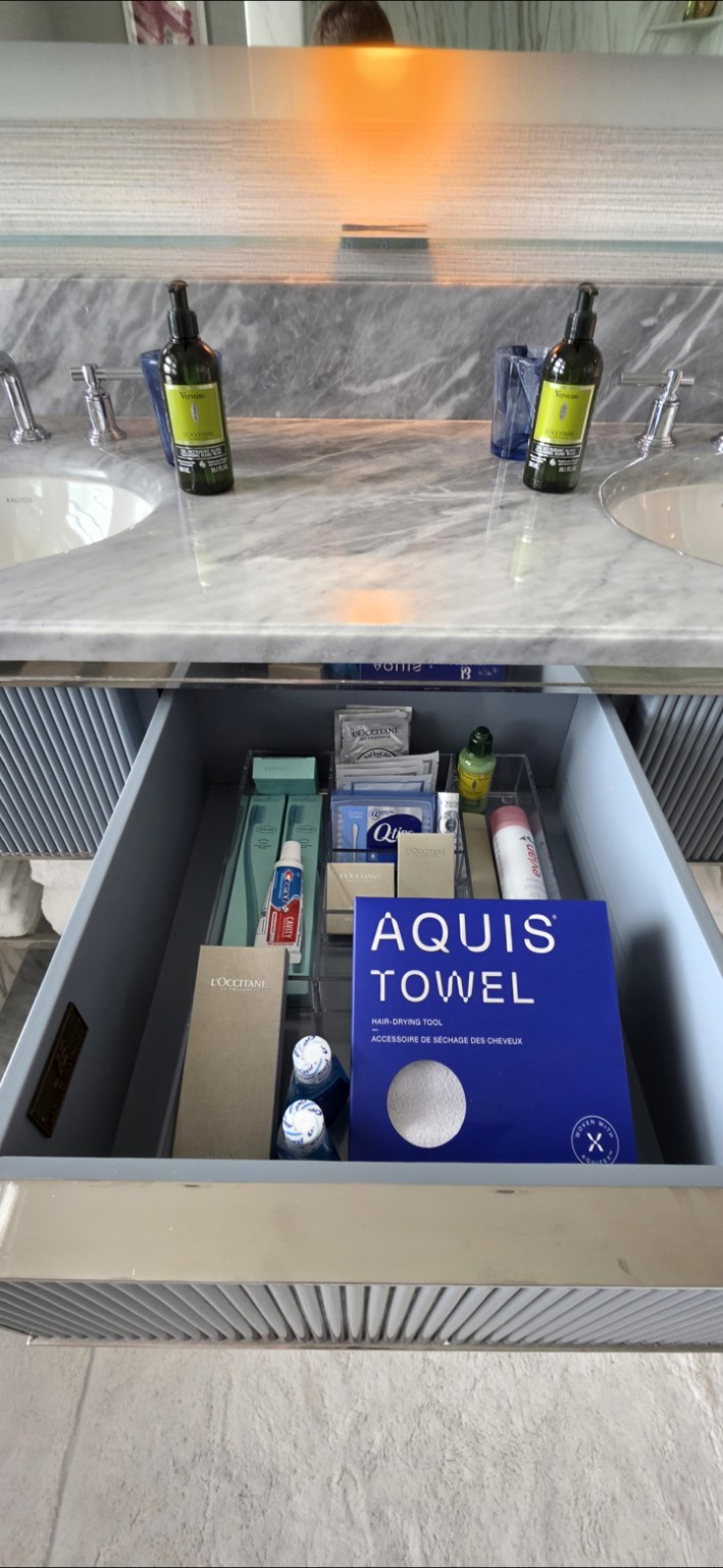 Open bathroom drawer stocked with L'Occitane toiletries, dental items, and an Aquis hair towel