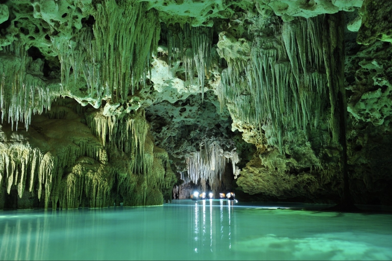 Green-lit stalactites and stalagmites above clear turquoise water inside Río Secreto