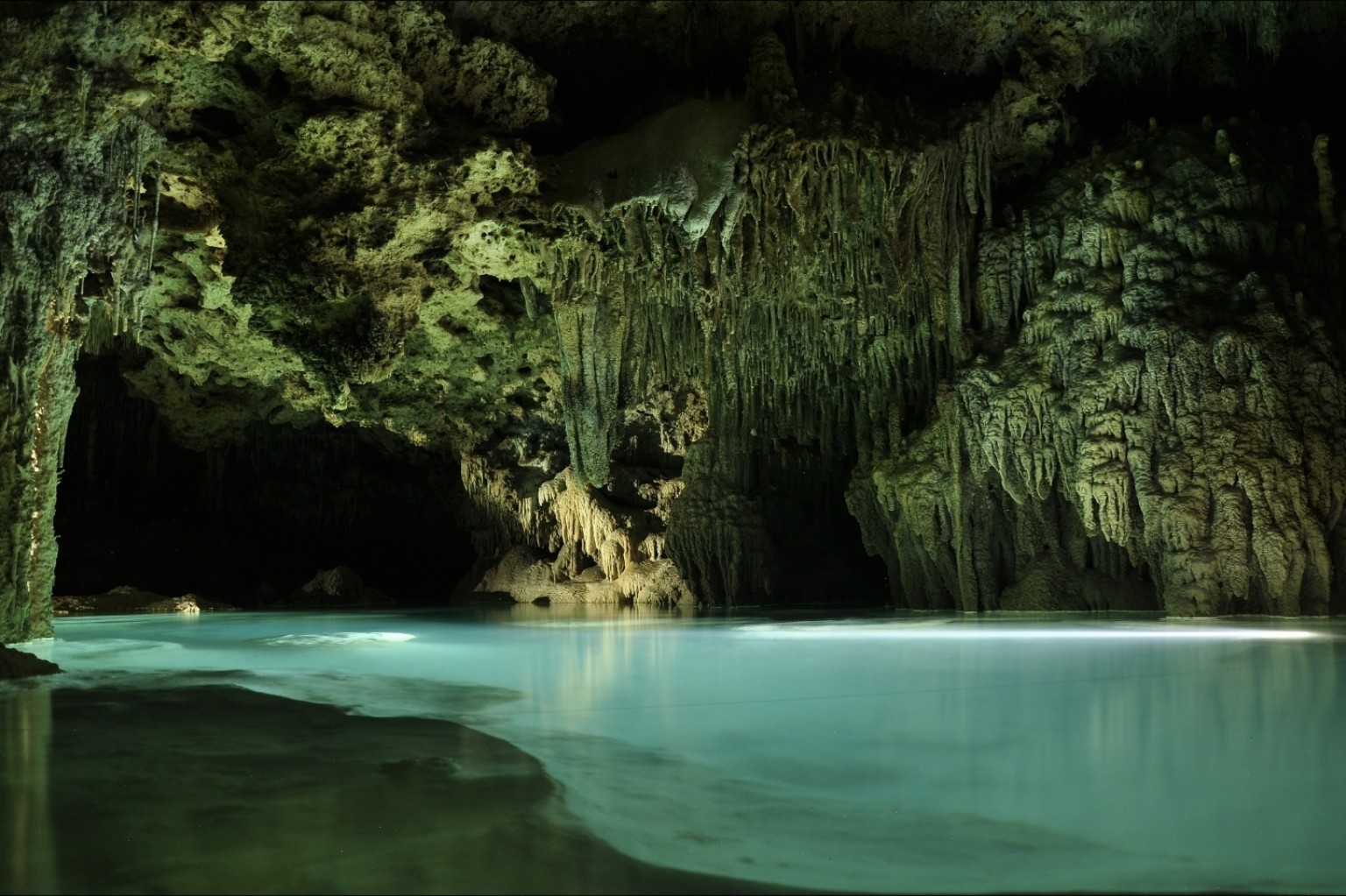 Turquoise underground river beneath dense stalactites and limestone formations at Río Secreto